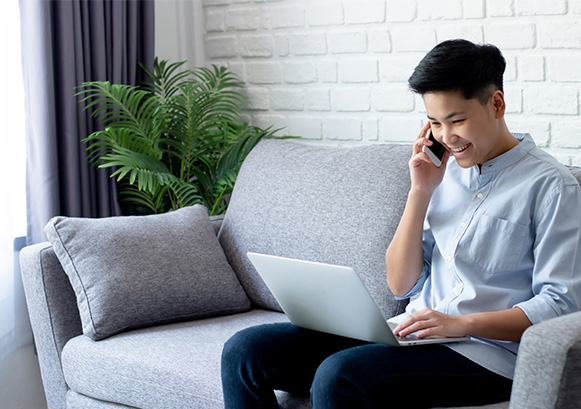 Man on  the phone on the sofa smiling and looking at his laptop