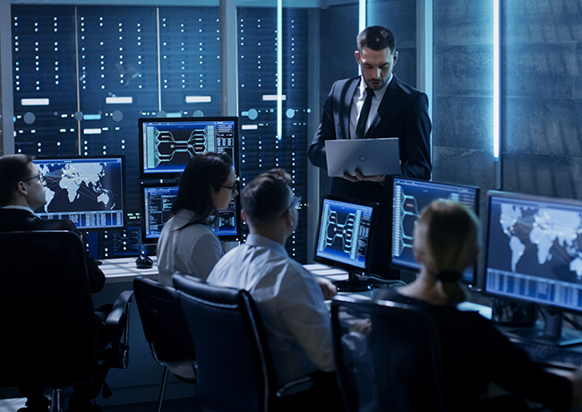 Technical man in suit on laptop with others at desk