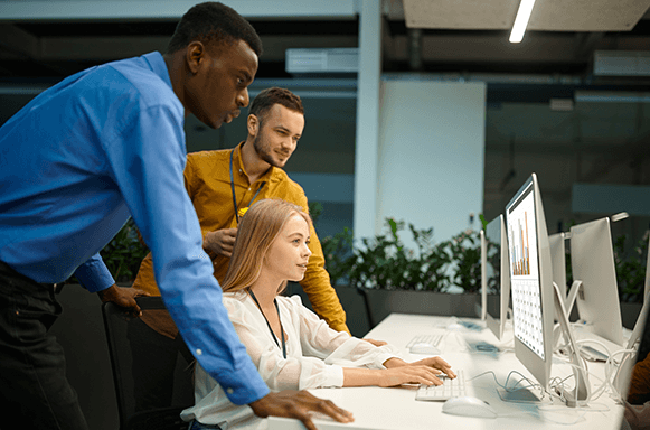 Three people huddled around a desktop computer screen