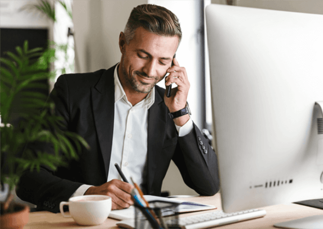 Smart man on phone reading at desk with laptop